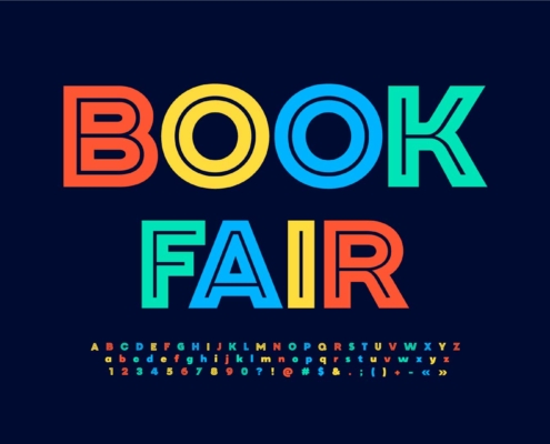 Text on the image reads "BOOK FAIR" in bold, colorful letters (red, yellow, blue, and green) on a dark blue background. Below the main text, there's a small sample of the alphabet in uppercase and lowercase letters, as well as numbers and symbols, all in matching colors.