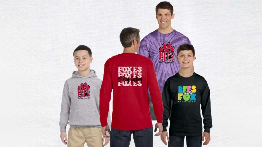 Four individuals modeling Ring Factory Elementary spiritwear. From left to right: a child wearing a gray hoodie with a red paw print and "RFES," a person in a red long-sleeve shirt with the word "Foxes" repeated on the back, a man in a purple tie-dye shirt with the same paw print and "RFES" logo, and another child in a black long-sleeve shirt with colorful text that reads "RFES Vibes Fox."